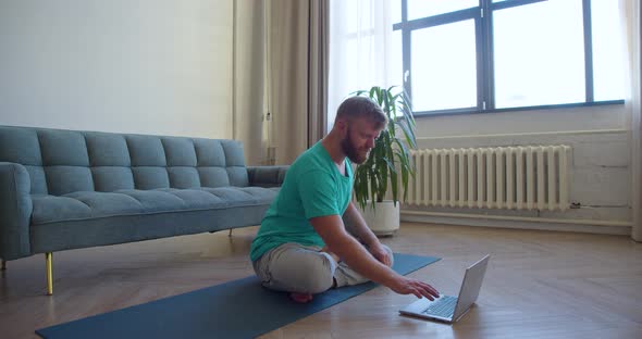 Middleaged Man Taking an Online Yoga Class  He Meditating on the Floor in Front of a Laptop Monitor