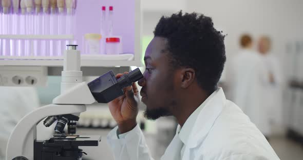 Africanamerican Man Making Medical Research Using Microscope Working in Lab