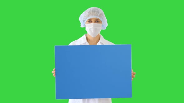 Woman Doctor in a Mask Holding an Empty Board on a Green Screen, Chroma Key.