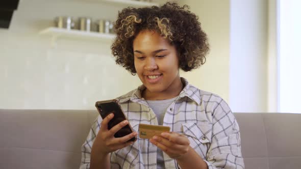 A Happy Young AfricanAmerican Woman Pays Through Her Smartphone at Home