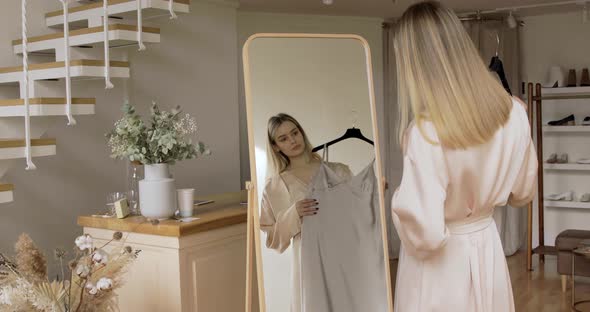 Sensual Girl With Blond Hair Is Trying On A Silk Dresses In Front Of The Mirror