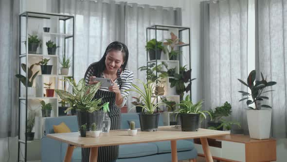 Smiling Asian Woman Holding Smartphone And Taking Photos Of Plants At Home