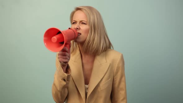 Beautiful woman in jacket with megaphone on blue background