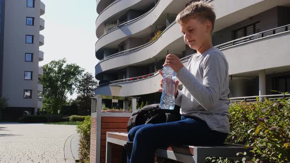 Schoolboy Takes Bottle Out of His School Backpack and Drinks Water