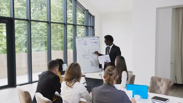 Male American African Manager Presents on Whiteboard New Project Plan to Colleagues at Meeting
