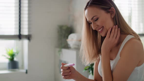 Cheerful woman standing and holding a pregnancy test. Shot with RED helium camera in 8K.