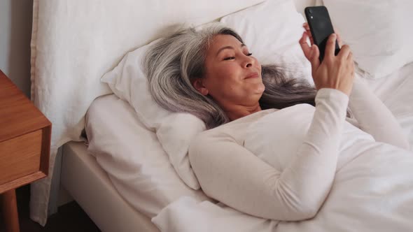 Positive Asian woman typing by phone