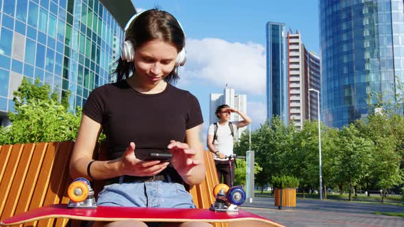 A Girl with a Skateboard Uses a Mobile Phone