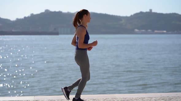 Side View of Sporty Young Woman Jogging Along Embankment