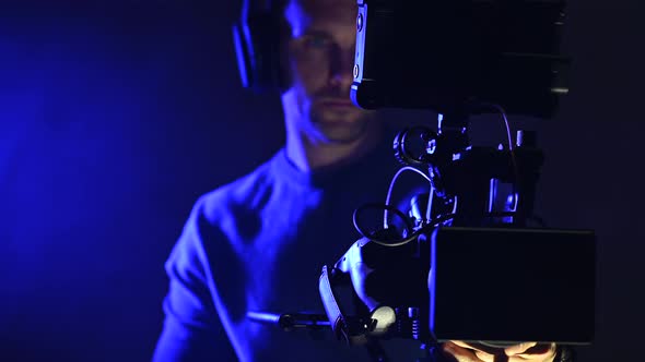 Caucasian Digital Film Camera Operator in Dark Blue Illuminated Place