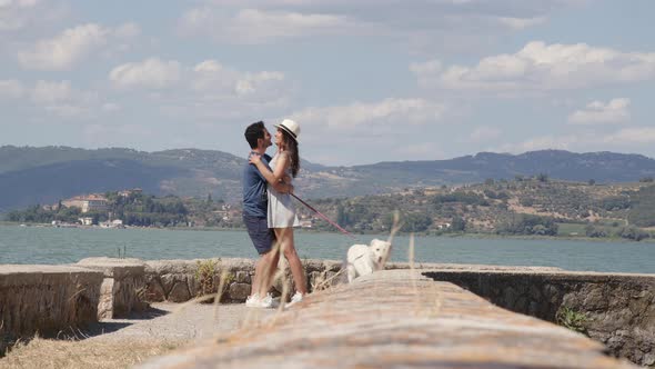 Couple with dog kissing on mole at lake in summer