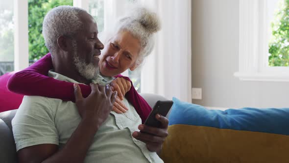 Mixed race senior couple using smartphone in the living room at home