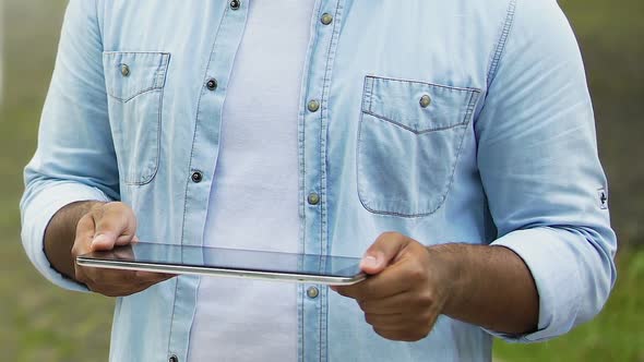 Male freelancer working on tablet outdoors, hands zooming files on touchscreen