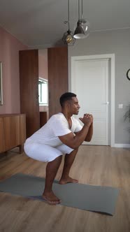 Side View of AfricanAmerican Man Exercising and Making Squats During Working Out at Living Room