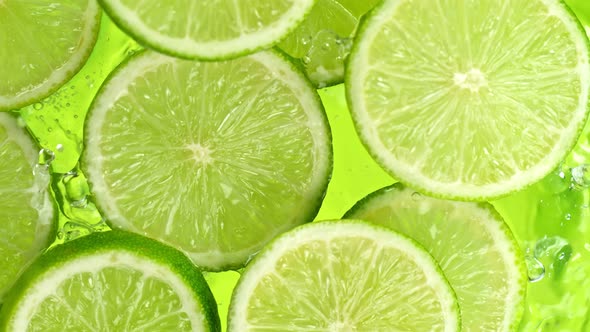 Super Slow Motion Shot of Lime Slices Falling Into Water on Green Background at 1000Fps