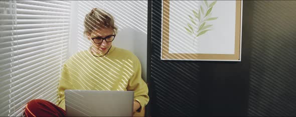 Woman Working on Laptop on Window Sill at Home