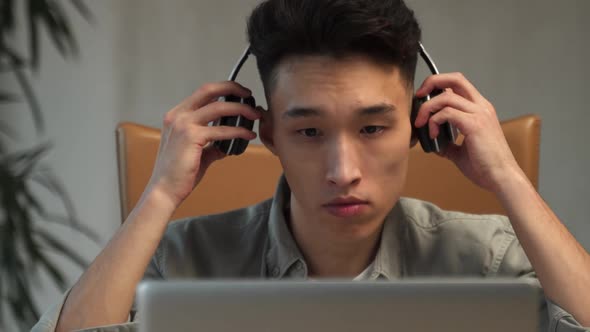 Young Asian Employee Puts on Headphones to Talk to Customer