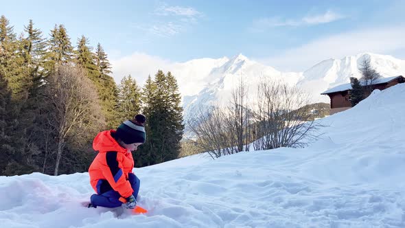 Boy Play Outside and Throw Snow with Shovel Over Mountains