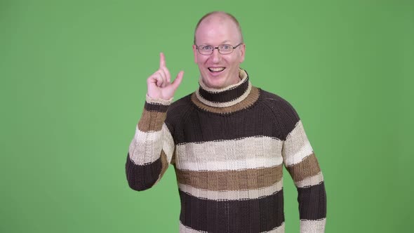 Happy Mature Bald Man with Turtleneck Sweater Pointing Up