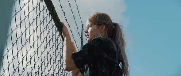 Young woman climbing on metal fence while looking back