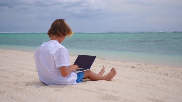 A Student is Engaged in Selfeducation Sitting on the Beach Against the Background of the Turquoise