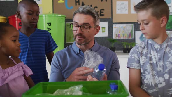 Diverse teacher and schoolchildren standing in classroom learning about recycling trash