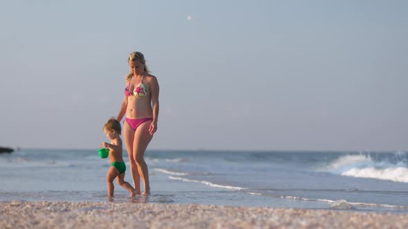 Mom Walks Along the Sea Beach with Her Son Collecting Seashells Under the Summer Sun