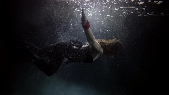 Slim Woman Is Floating Underwater in Darkness and Depth Subaquatic Shot