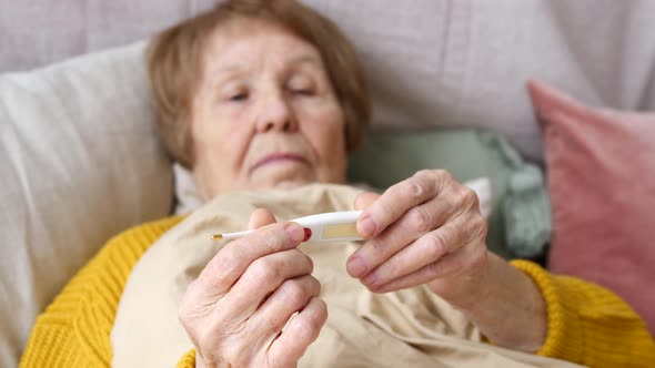 Sick Senior Woman Checking Thermometer On Bed At Home