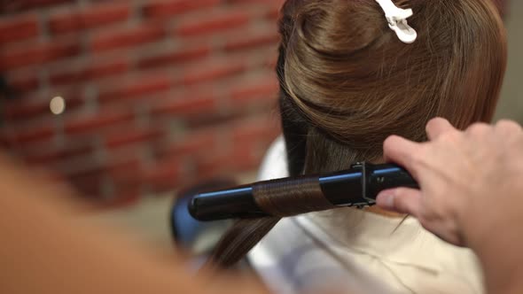 Closeup Male Hairstylist Using Curling Iron in Beauty Salon Doing Hairdo for Female Client