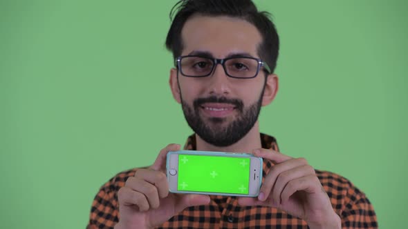 Face of Happy Young Bearded Persian Hipster Man Thinking While Showing Phone