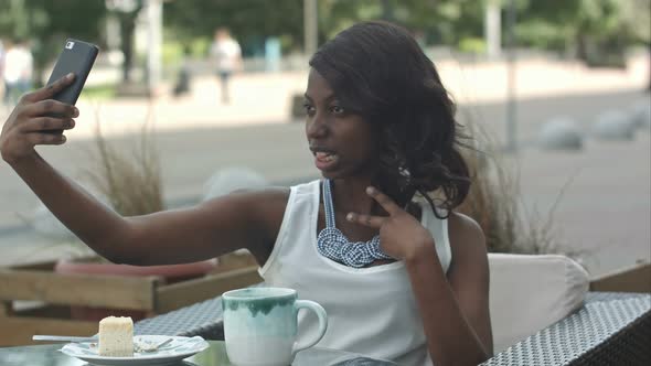 Attractive Young African Woman Smiling and Taking a Selfie with Her Smartphone While Sitting Alone