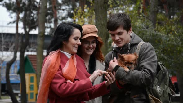 Group of People a Woman a Girl and a Guy with a Dog are Watching Something on a Smartphone