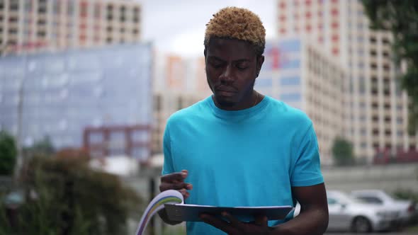 Concentrated Intelligent African American Man Analyzing Paperwork Standing in Urban City on Street