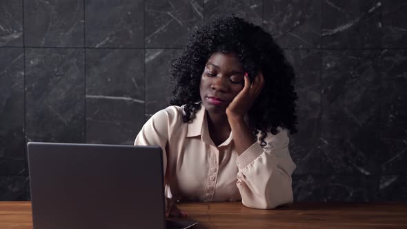 Black Businesswoman with Curly Hair Types on Laptop Lazily