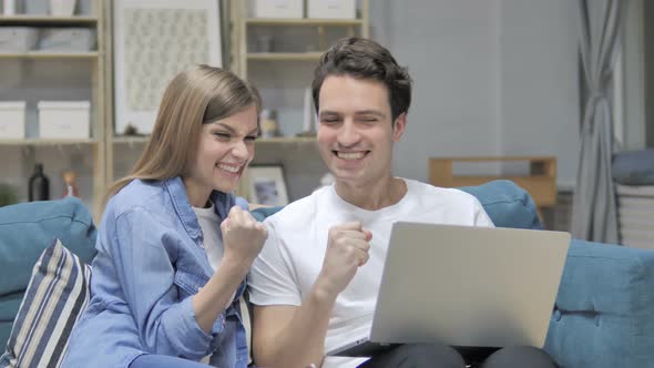 Excited Young Couple Celebrating Success While Using Laptop