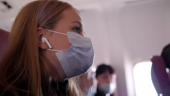 A Woman in a Mask Putting on Wireless Headphones in an Airplane During Flight