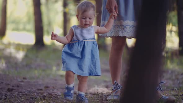 mother with a one-year-old child walks through the woods or park. first steps of the child