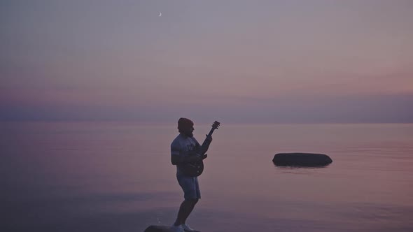 Alone Guy Plays the Guitar While Standing on a Stone. Hipster Man Enjoying a Song in the Middle of