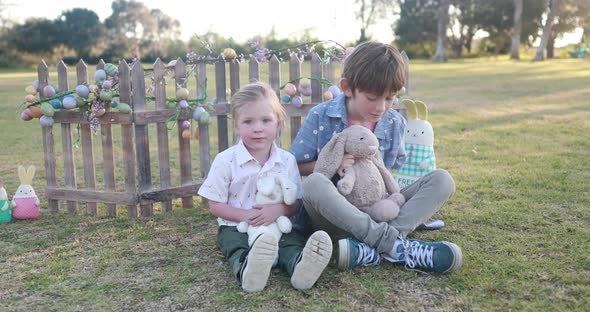 Two brothers wearing Easter themed clothes hold and hug stuffed Easter bunnies and smile.