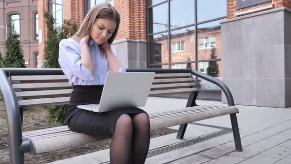 Tired Young Woman Sitting Outside Office Working on Laptop