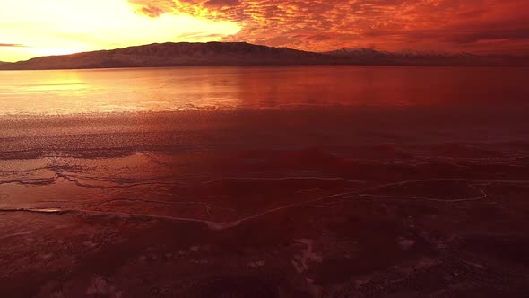 Flying backwards from ice on lake to higher aerial view of colorful sunset