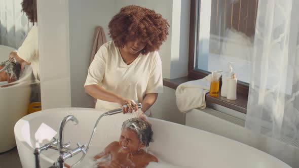 African American Mother Washing Hair of Little Son in Bathroom