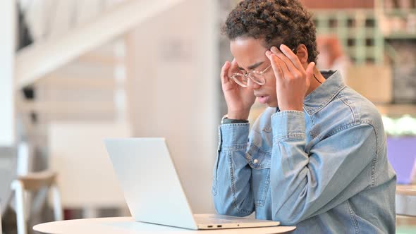 Stressed African Woman with Laptop Having Headache at Cafe 