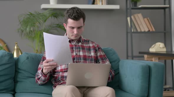 Man with Laptop Working on Documents on Sofa