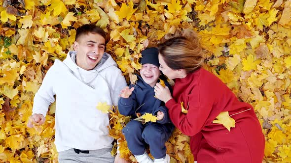 Happy Family Play Lying on Ground Covered with Yellow Leaves