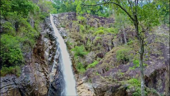 Drone Flies Closely From Lake To Waterfall Top Among Trees
