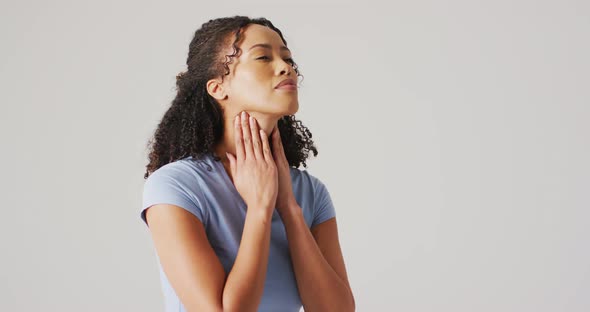 Video of biracial woman touching her neck on white background