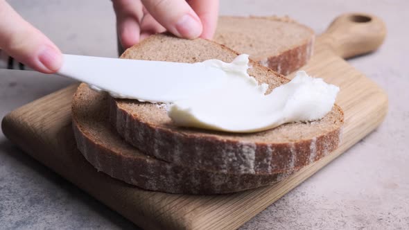 Spreading rye bread toast with cream cheese.