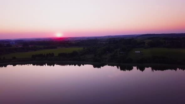 Colorful sunset over a peaceful lake, sarrounded by trees. Drone shot. Relaxing scenery.